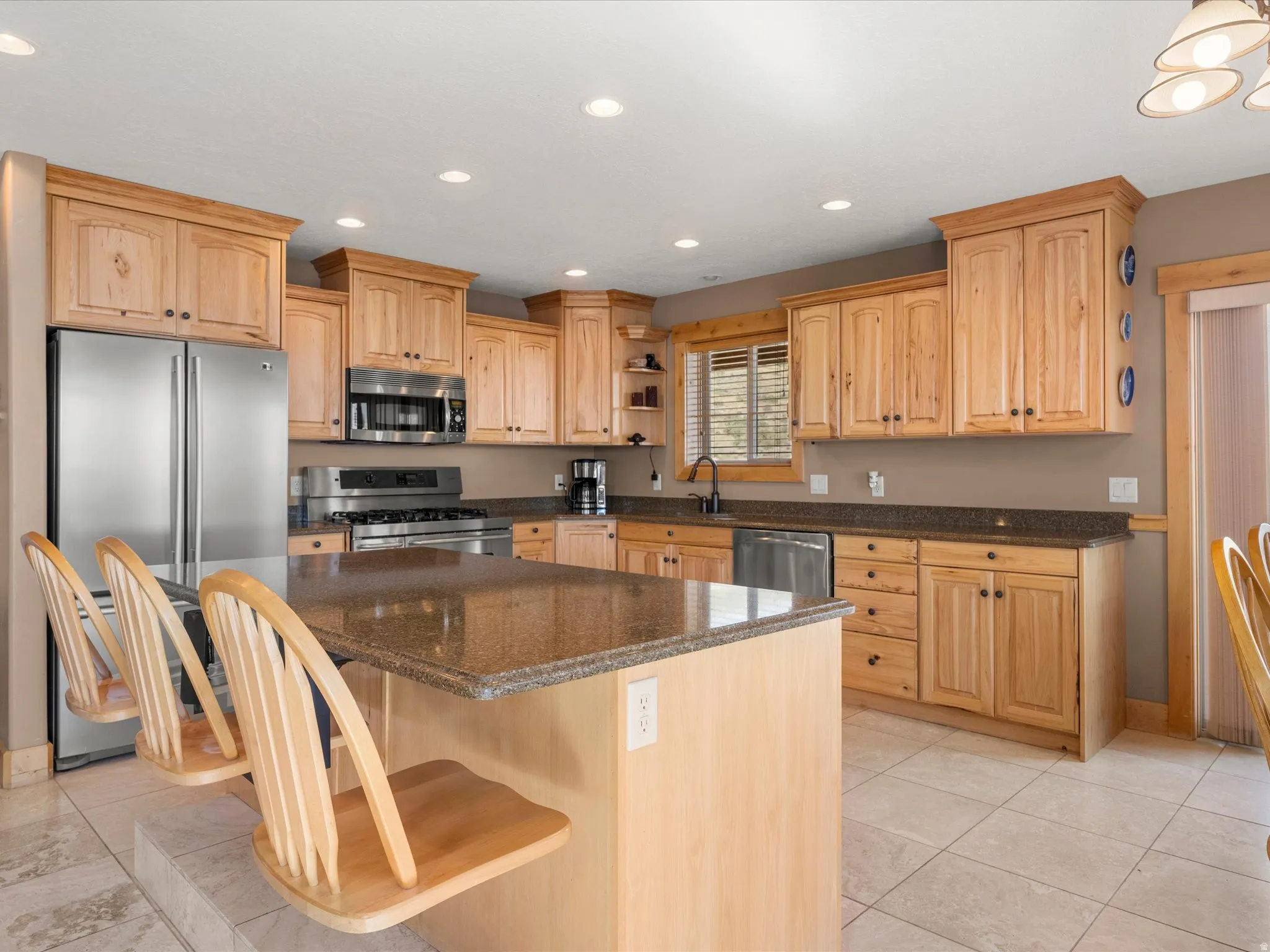 Kitchen featuring light wood cabinetry, stone countertops, stainless steel appliances, a center island with bar seating, and recessed lighting