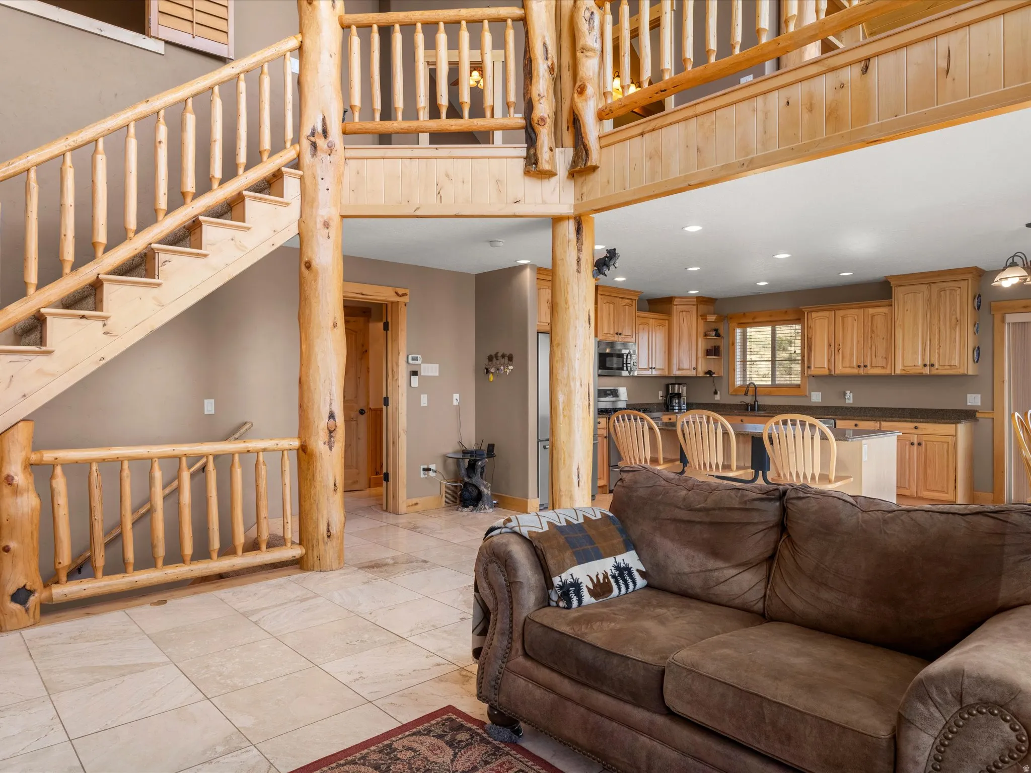 Open-concept living area with tiled flooring, a natural wood staircase, and a wood-finished kitchen featuring a breakfast bar and recessed lighting