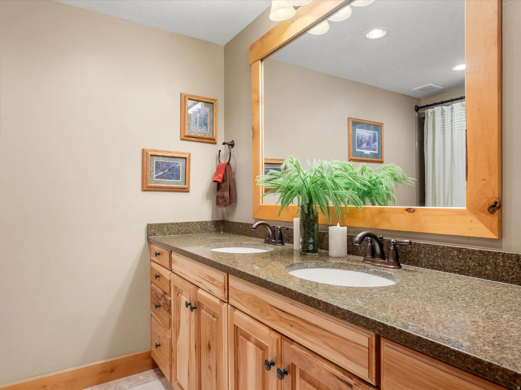 Double vanity with wood-finish cabinetry, integrated sinks, bronze-finish faucets, and a large framed mirror