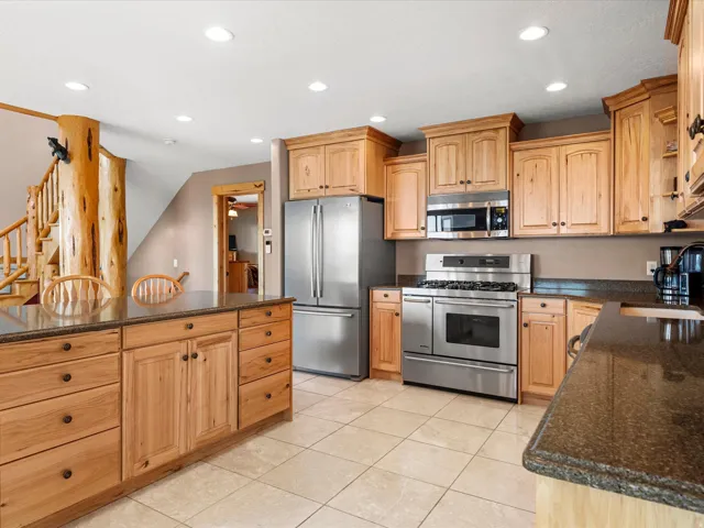 Kitchen featuring stainless steel appliances, wood cabinetry, stone countertops, and tile flooring