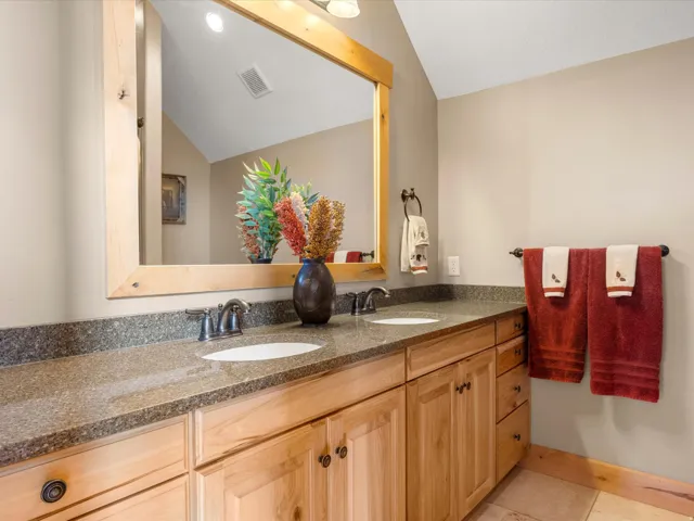 Double vanity with light wood cabinetry, stone-finish countertop, and undermount sinks