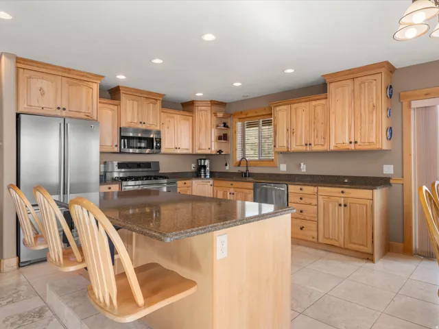 Kitchen featuring light wood cabinetry, stone countertops, stainless steel appliances, a center island with bar seating, and recessed lighting