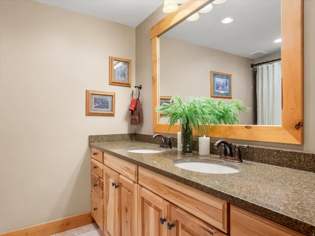 Double vanity with wood-finish cabinetry, integrated sinks, bronze-finish faucets, and a large framed mirror