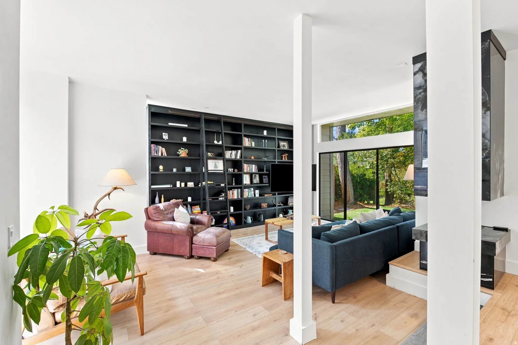 Light wood-finish flooring, extensive built-in shelving, a modern fireplace with stone surround, and expansive windows offering natural light