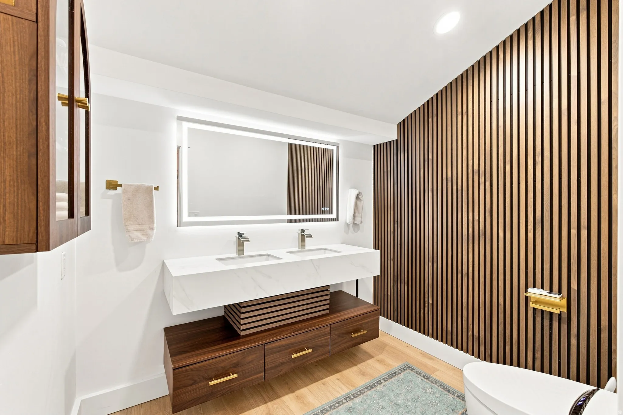 Dual vanity with undermount sinks, illuminated mirror, wood-finish panel accent wall, and recessed lighting