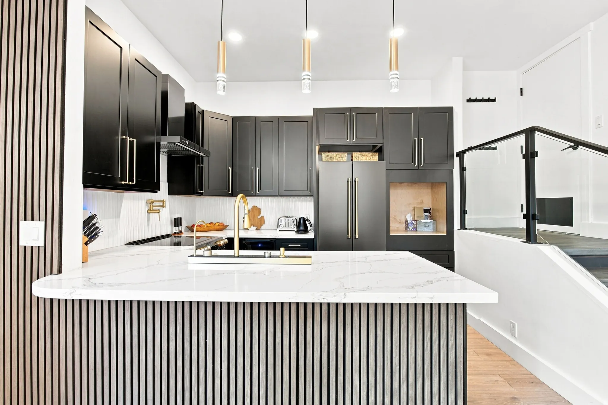 Modern kitchen featuring matte black cabinetry with gold-toned hardware, a white countertop with integrated sink, and an integrated refrigerator