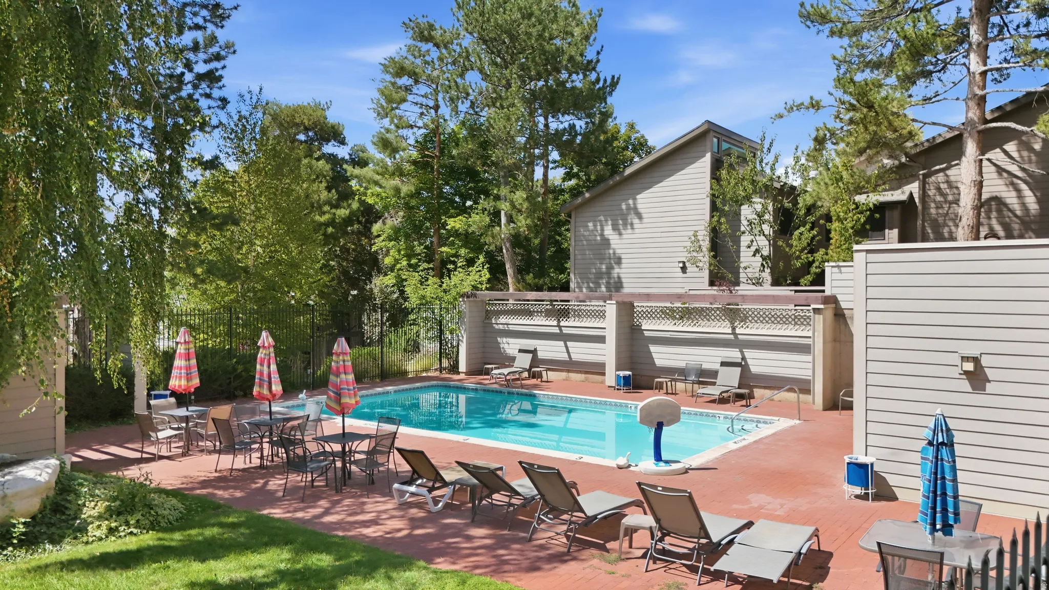 Outdoor swimming pool with a red brick patio surround, framed by mature trees and a privacy fence