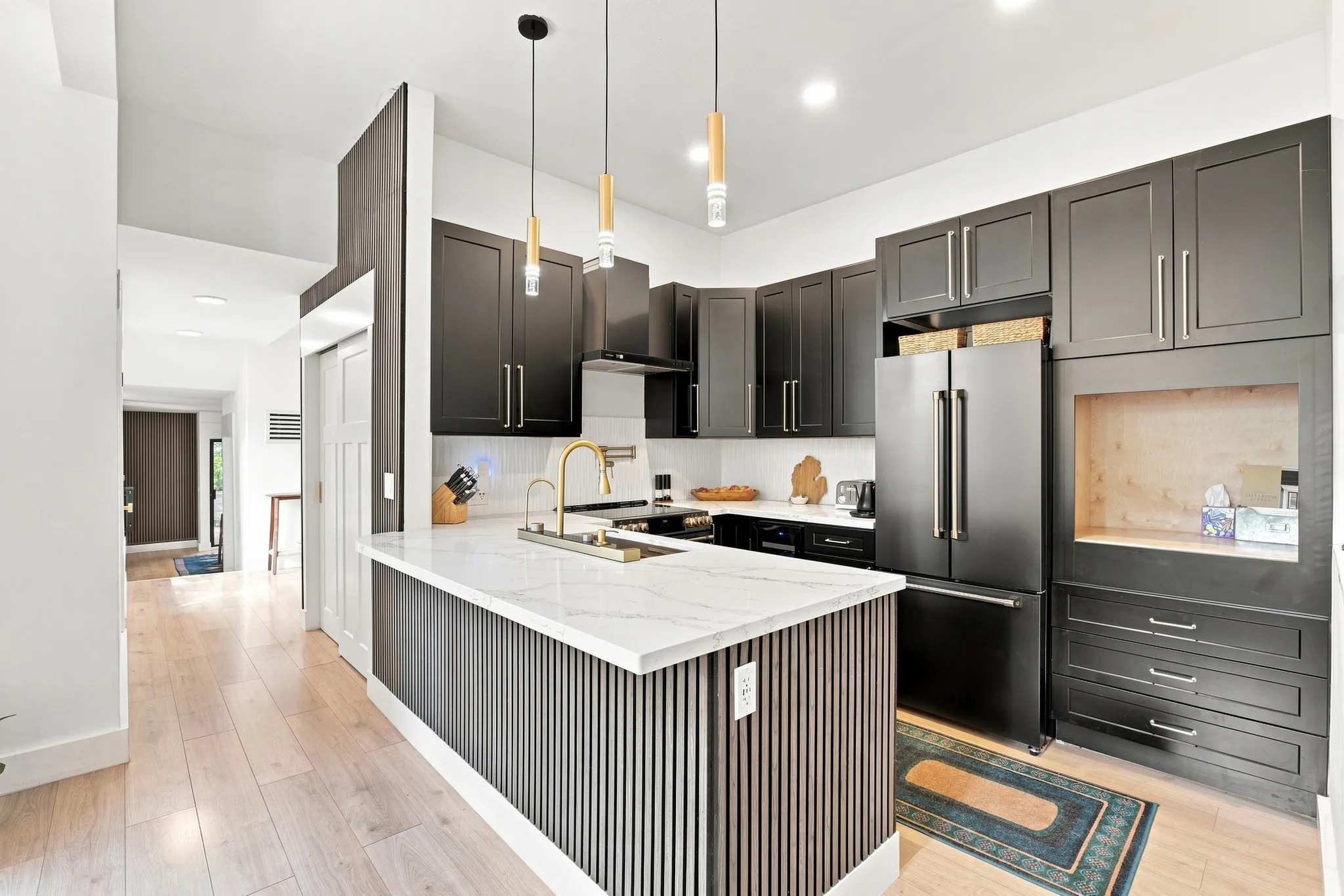 Kitchen featuring dark cabinetry, a white countertop island with slatted detailing, a gold-finish faucet, and integrated appliances