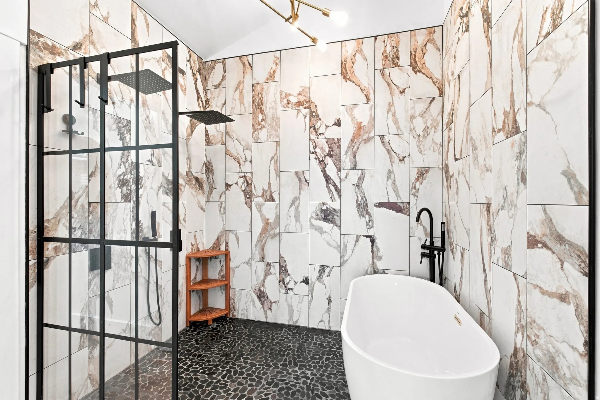 Freestanding soaking tub, black pebble flooring, marble-look wall tiling, and a black-framed glass shower enclosure with dual showerheads