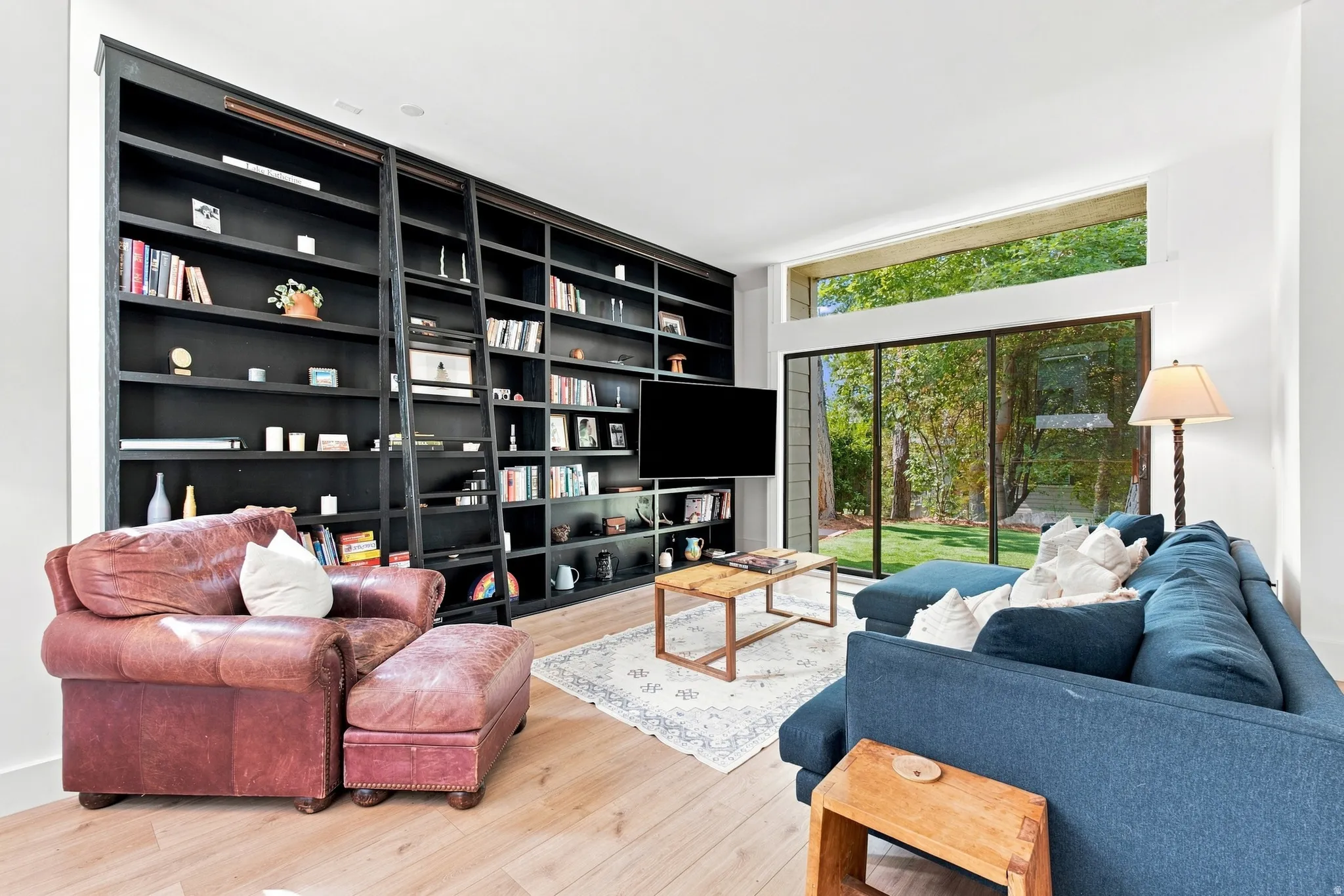 Expansive built-in shelving with rolling ladder, natural wood-finish flooring, and large picture windows