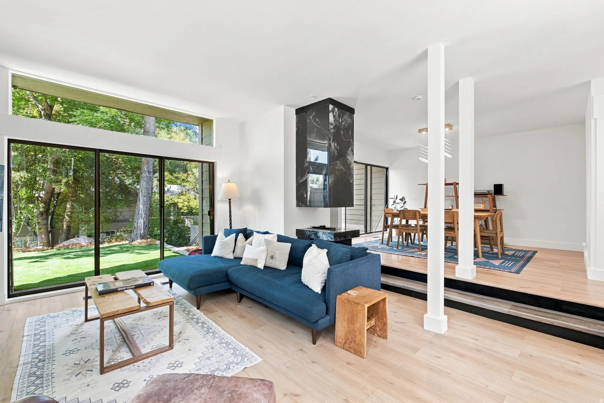 Spacious living area featuring light wood-finish flooring, a wall of sliding glass doors, a large transom window, and a built-in black marble-finish fireplace