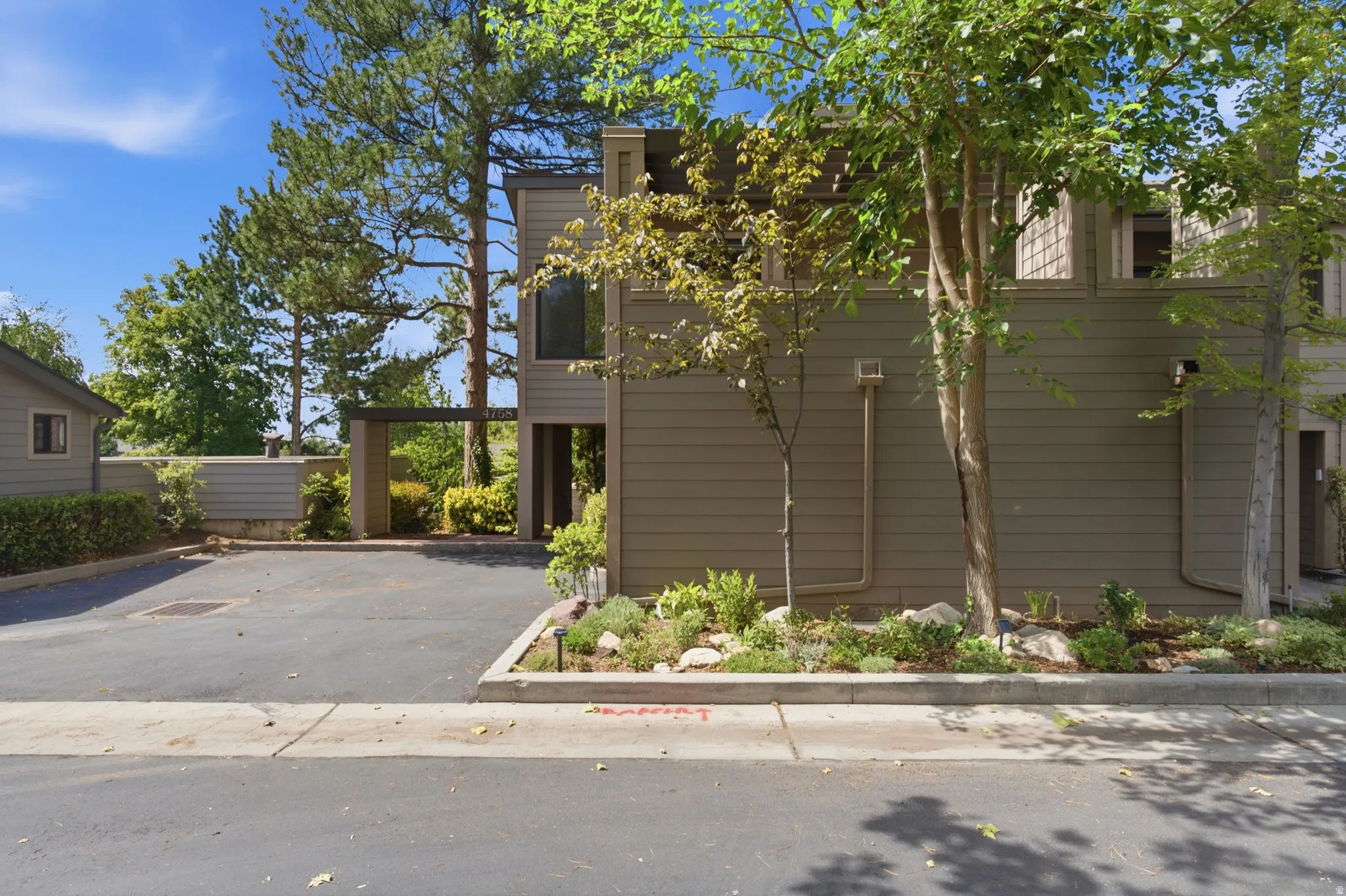 Siding exterior with multiple windows, mature trees, and a landscaped planting bed