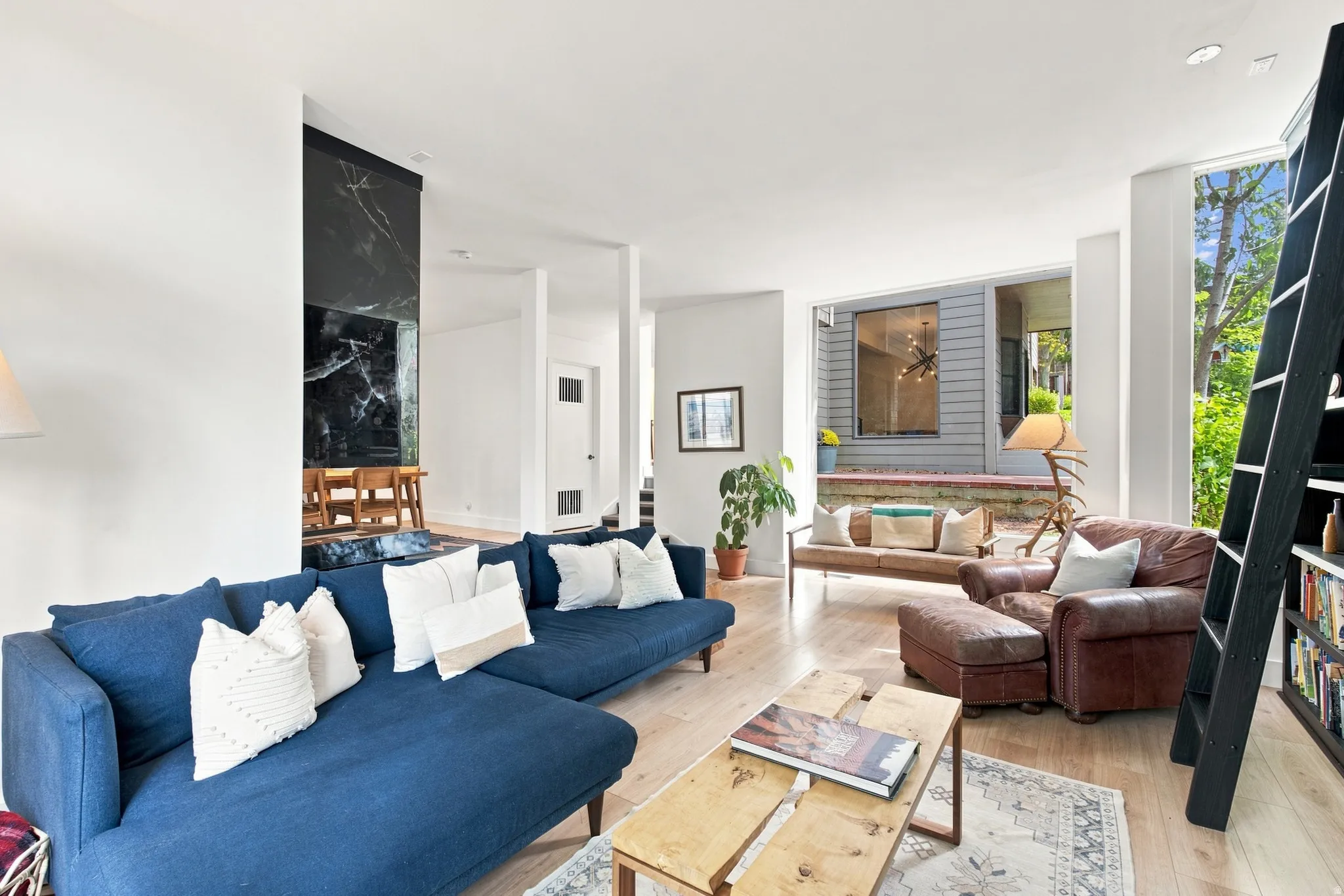 Open-concept living space featuring wood-finish flooring, a prominent black stone wall, recessed lighting, and large windows