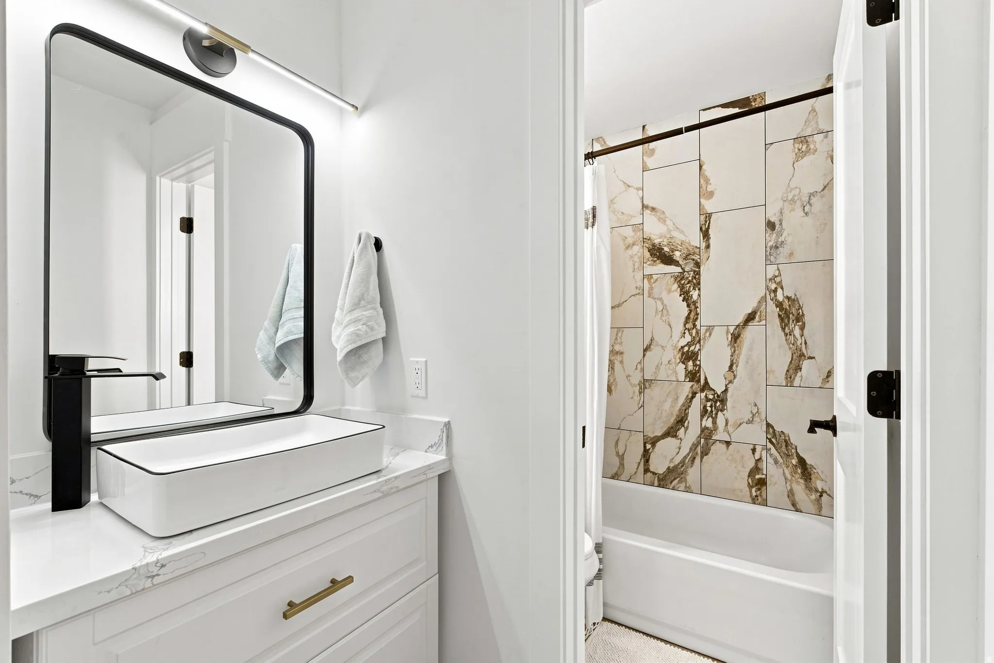 White shaker-style vanity with brass hardware, a solid surface countertop, and a rectangular vessel sink with a matte black faucet