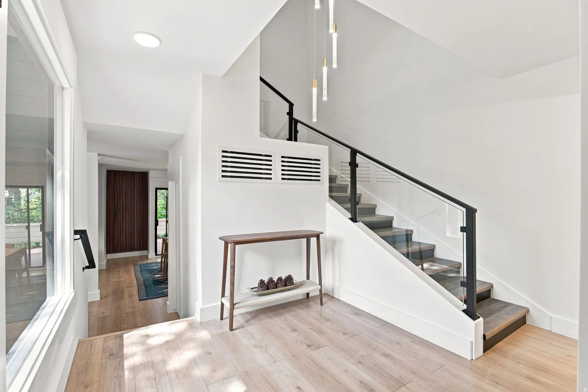 Light wood-finish flooring throughout, modern glass and black metal staircase railing, recessed lighting, and contemporary pendant lighting fixture