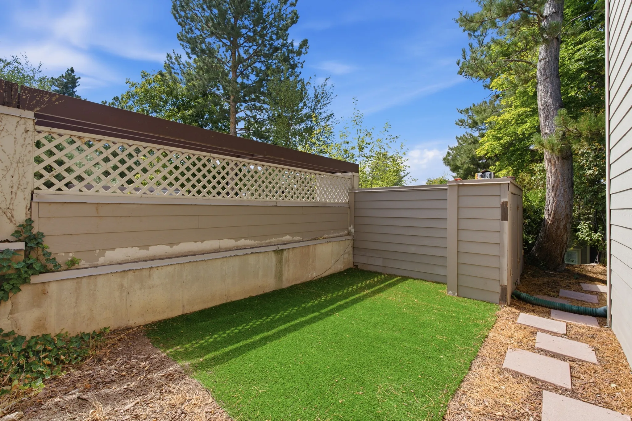 Private outdoor area featuring artificial turf, a decorative lattice fence, stone pavers, and mature trees