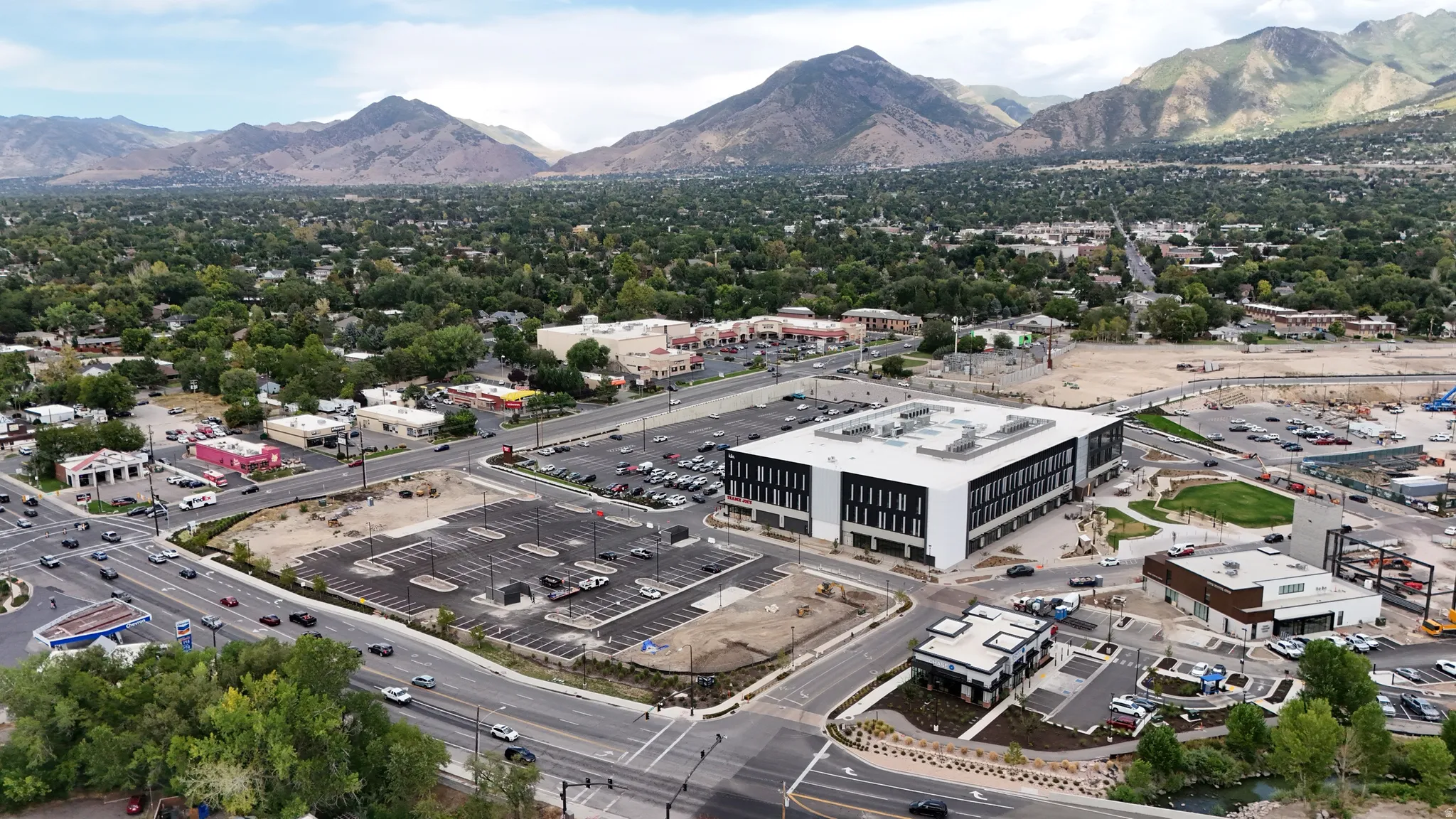 Aerial perspective showcasing a modern commercial building, extensive surface parking, and surrounding commercial infrastructure