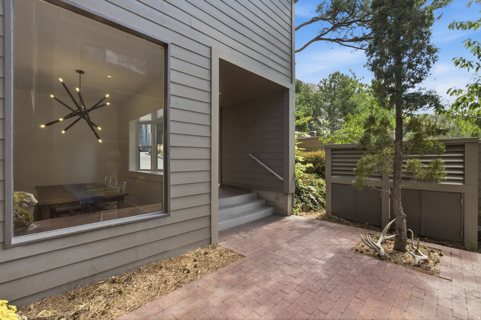 Exterior siding with a large picture window, brick paver patio, covered entry, and slatted privacy fencing