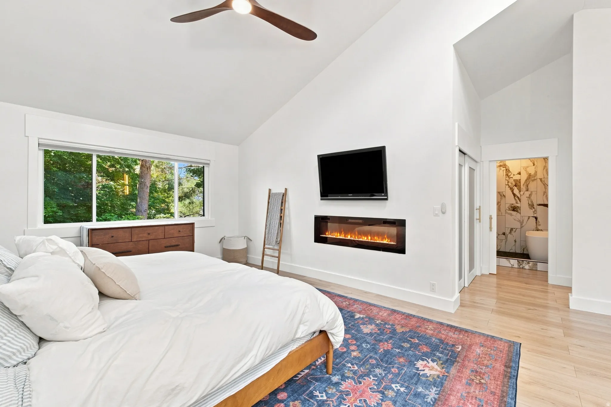 Vaulted ceilings, wood-finish flooring, large picture window, integrated electric fireplace, and a ceiling fan