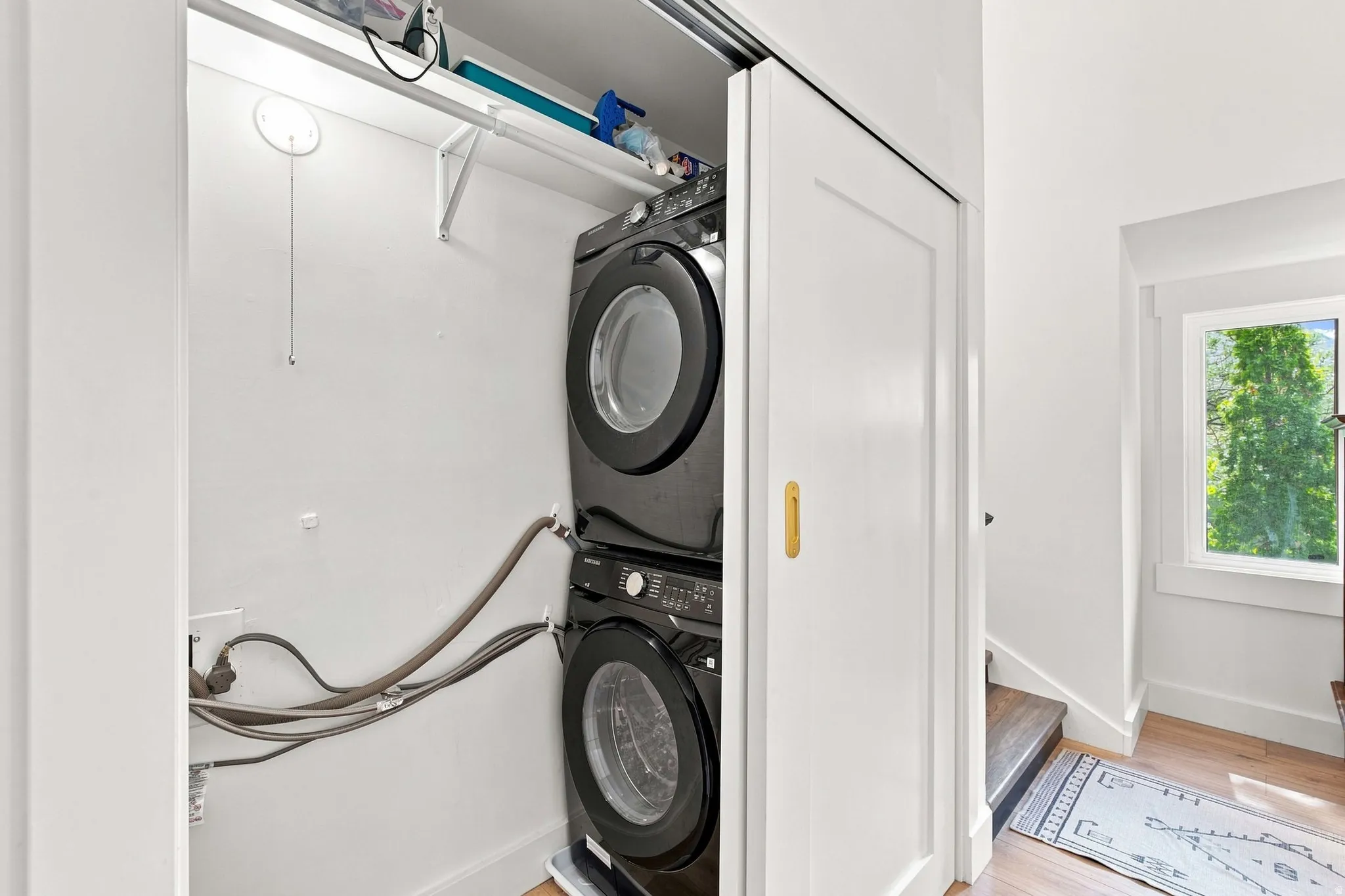 Built-in stacked laundry appliances within a closet, featuring a white bi-fold door with a gold-tone pull