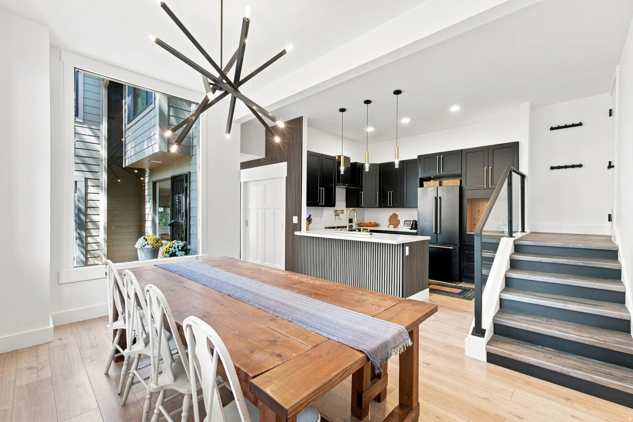 Open-concept area featuring light wood-finish flooring, a contemporary chandelier, and a black-finish kitchen with white countertops
