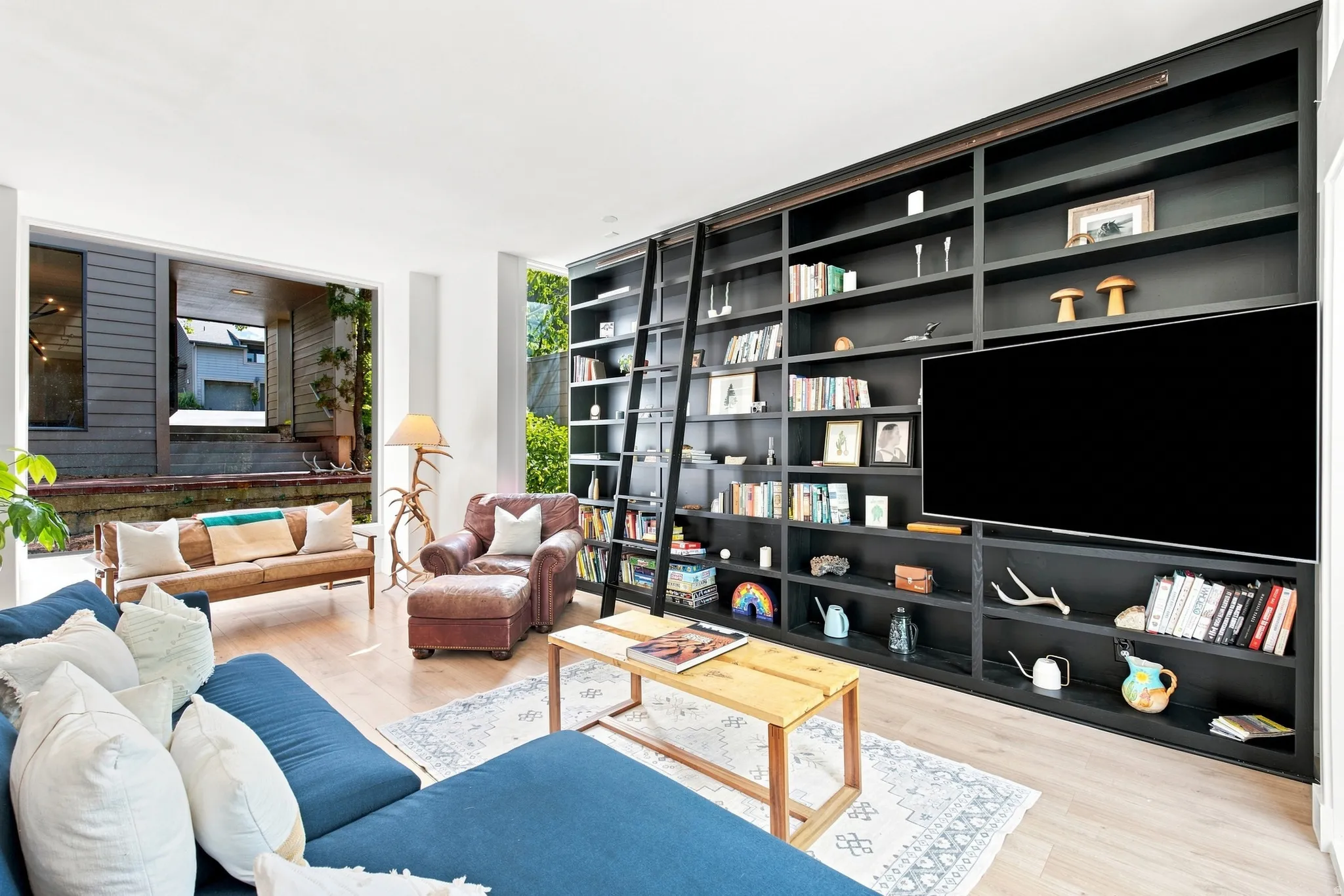 Wood-finish flooring with an expansive built-in shelving unit, integrated television, and a rolling ladder