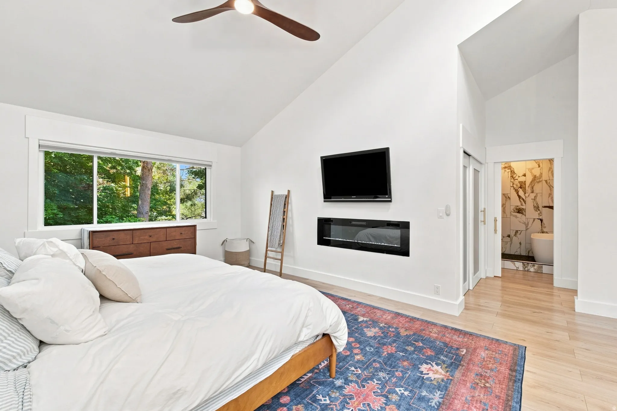 Vaulted ceiling, wood-finish flooring, large picture window, wall-mounted electric fireplace, and sliding glass panel door