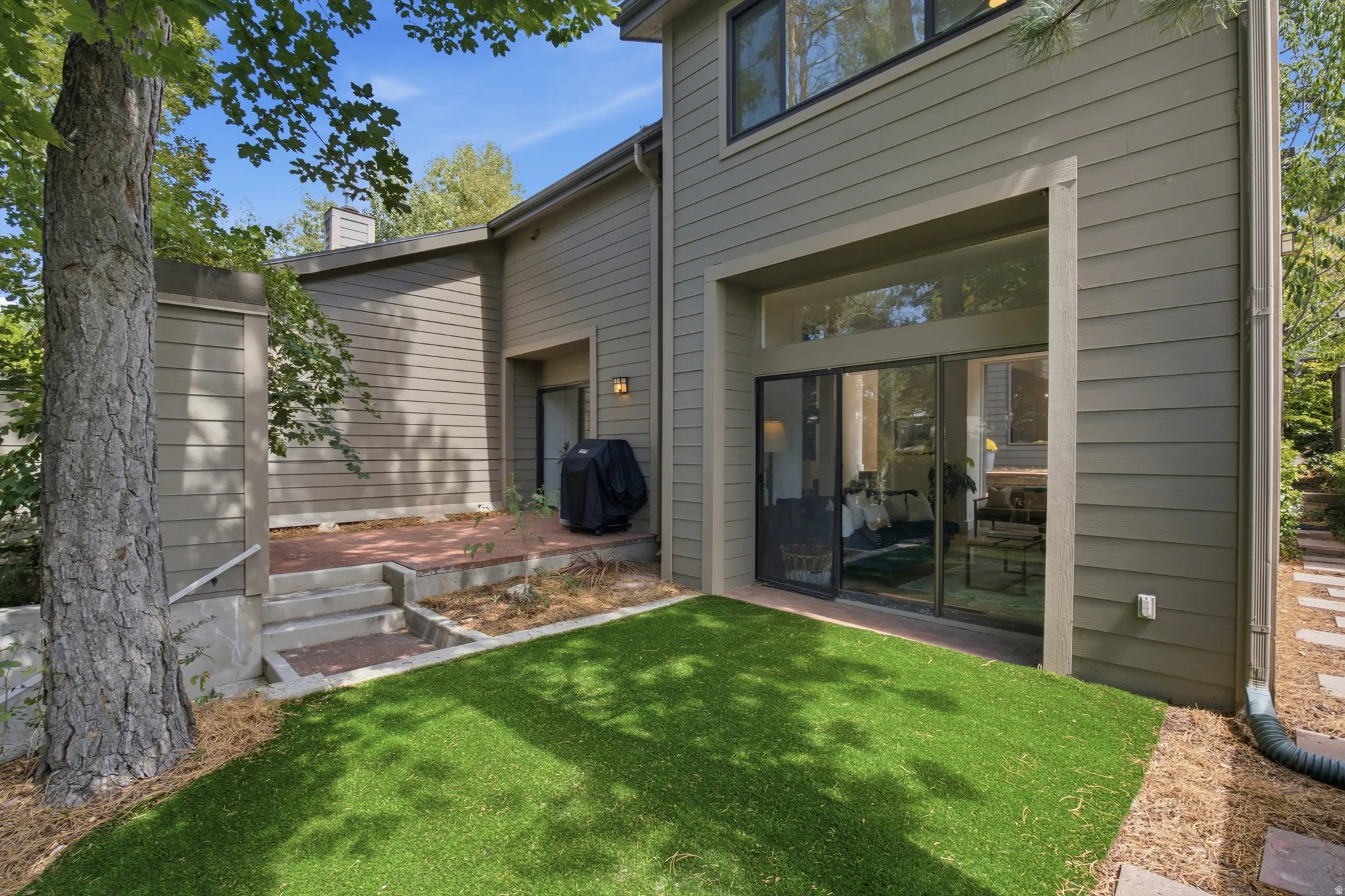 Sliding glass doors opening to an outdoor patio with artificial turf and flagstone steps