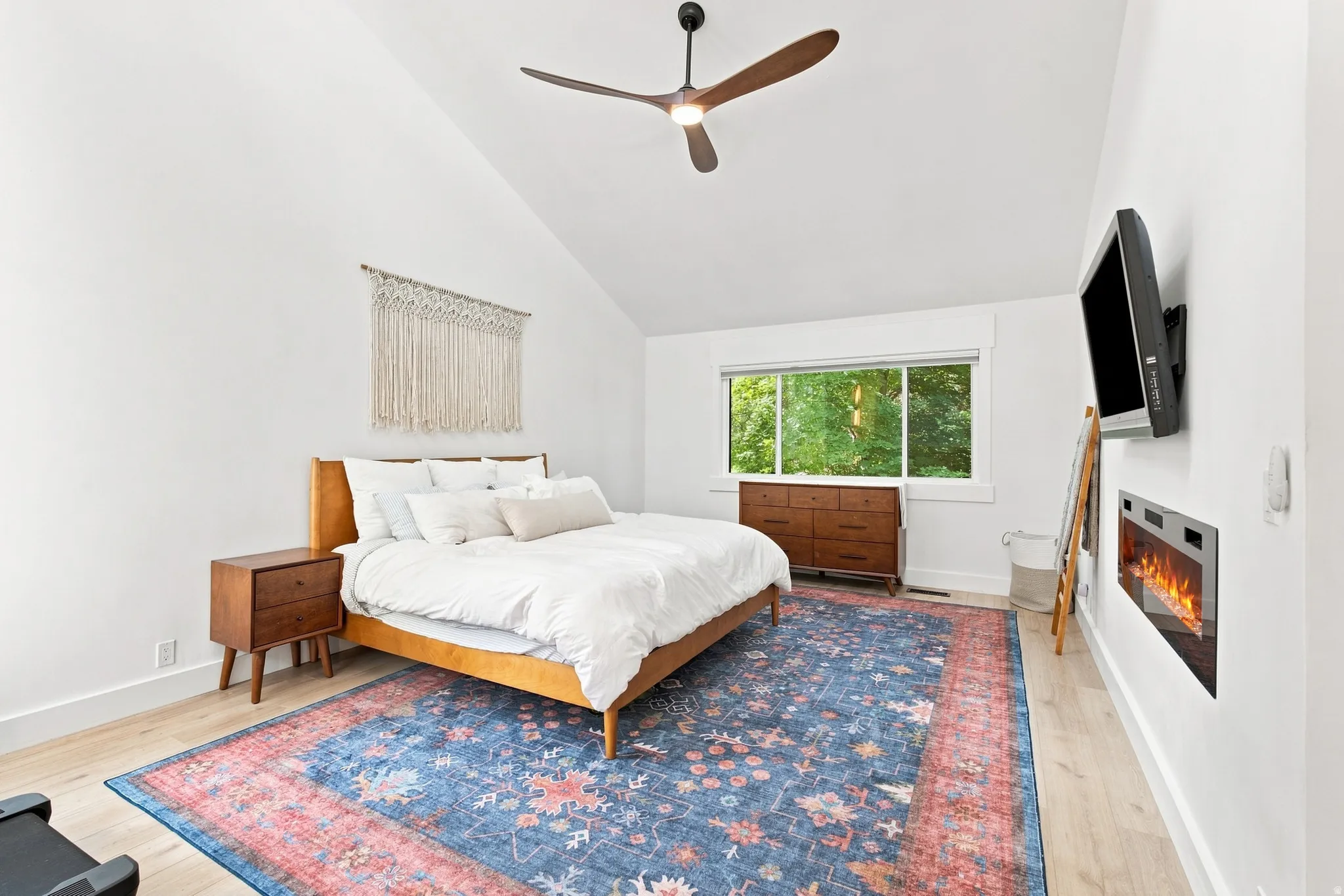 Vaulted ceiling, wood-finish flooring, built-in fireplace, large window, and ceiling fan