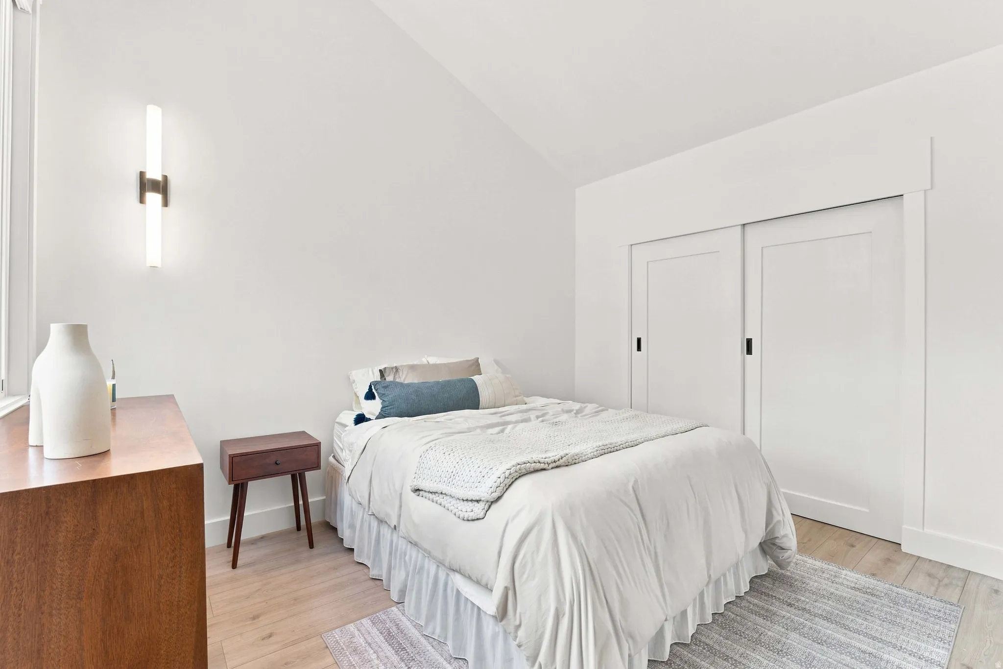Vaulted ceiling with an integrated wall sconce, wood-finish flooring, and sliding closet doors