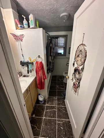 Bathroom featuring a single vanity with wood-finish cabinetry, a ceramic sink, a mirror, a window, and dark patterned tile flooring