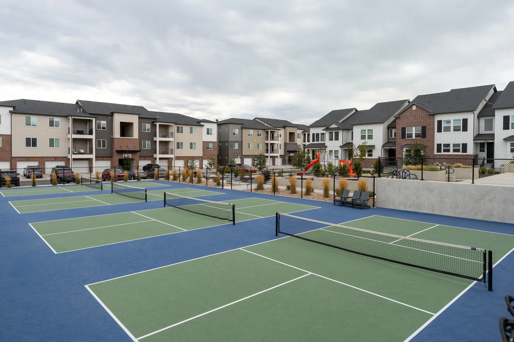 Multiple pickleball courts, playground structure, and community buildings with varied facades