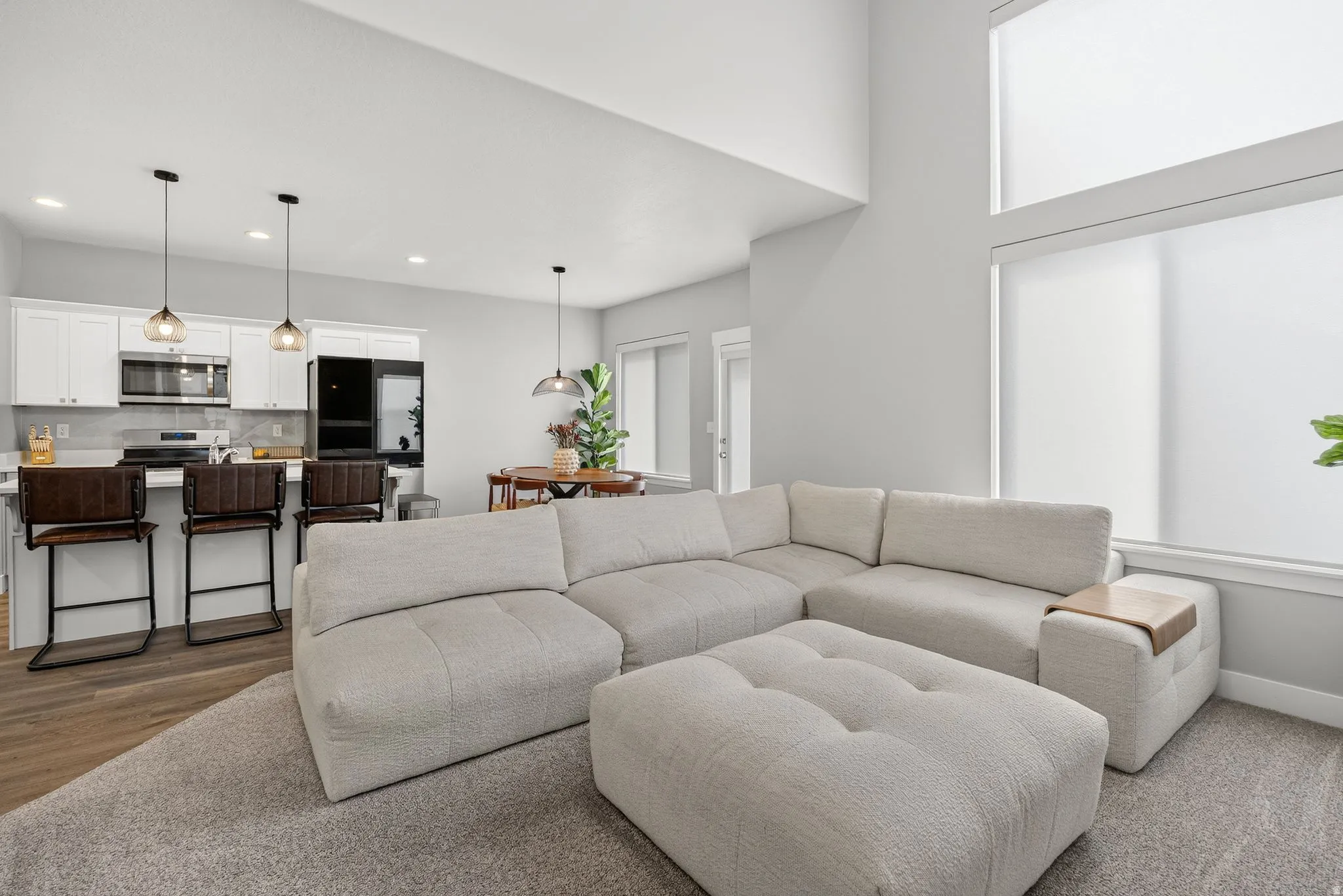 Two-story ceiling, large windows with roller shades, wood-finish flooring, white cabinetry, and stainless steel appliances