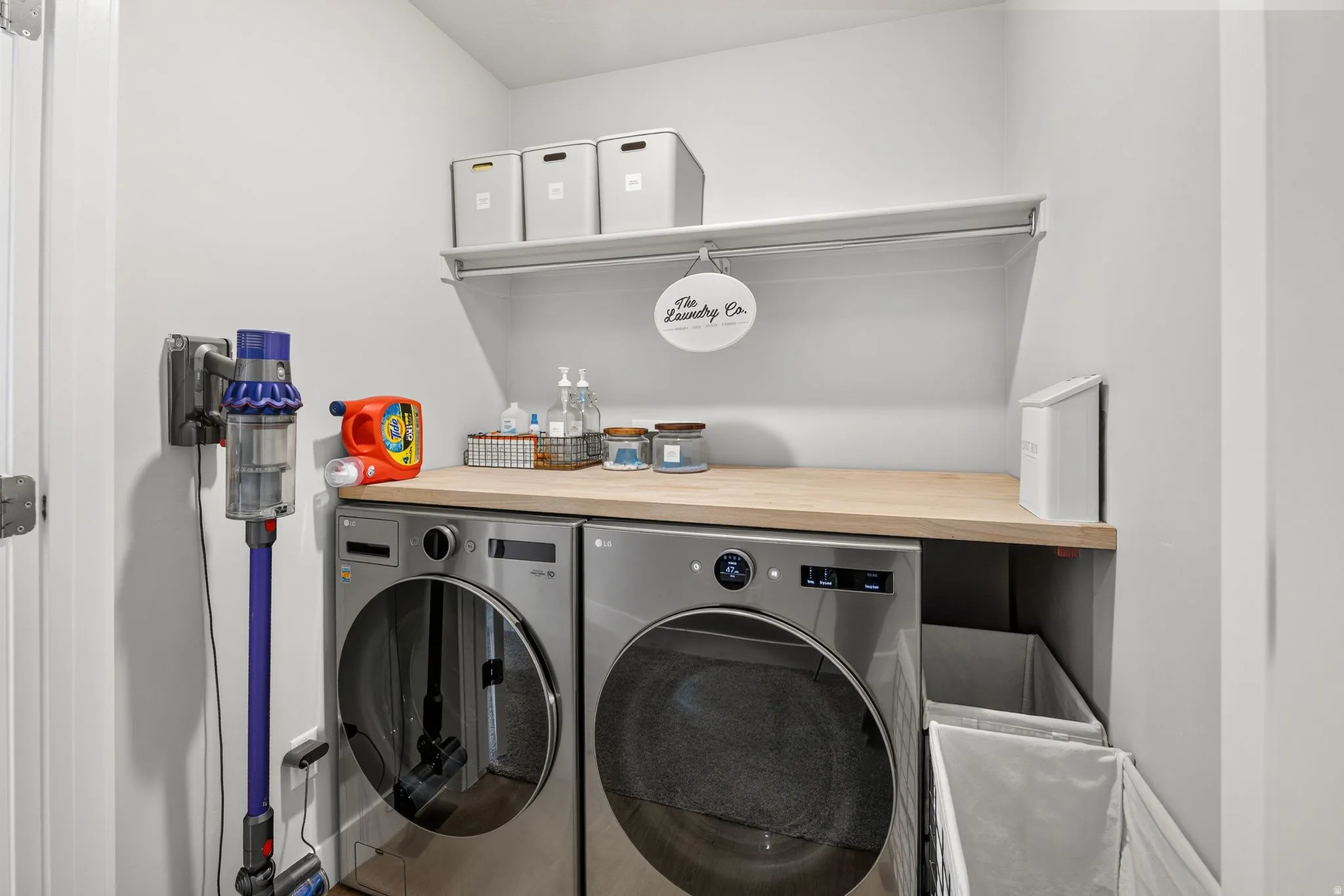 Full-sized laundry appliances with a wood-finish countertop, white wall shelving, and light gray walls