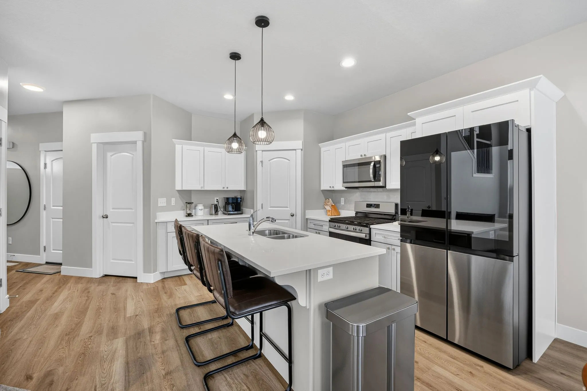 Kitchen with a large island, white cabinetry, integrated stainless steel appliances, and wood-finish flooring
