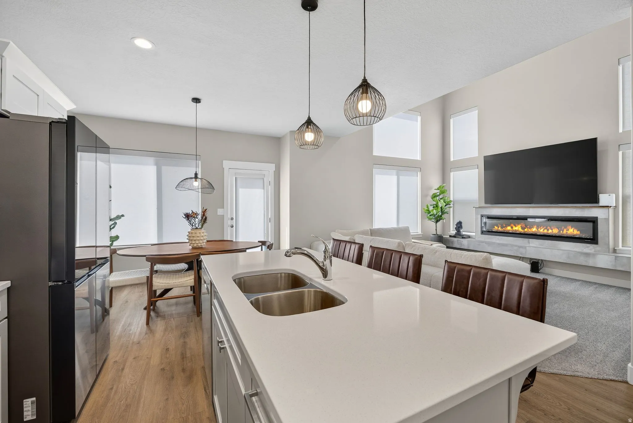 Kitchen island with double basin sink, wood-finish flooring, vaulted ceilings, modern linear fireplace, and large windows