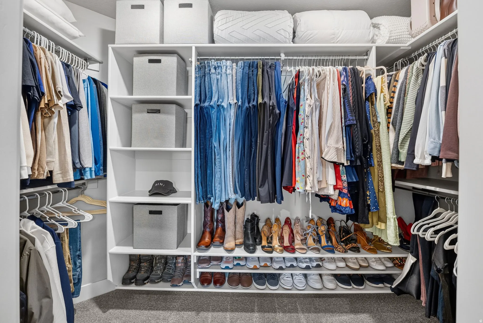 Built-in closet system featuring multiple hanging rods, white shelving, and carpet flooring