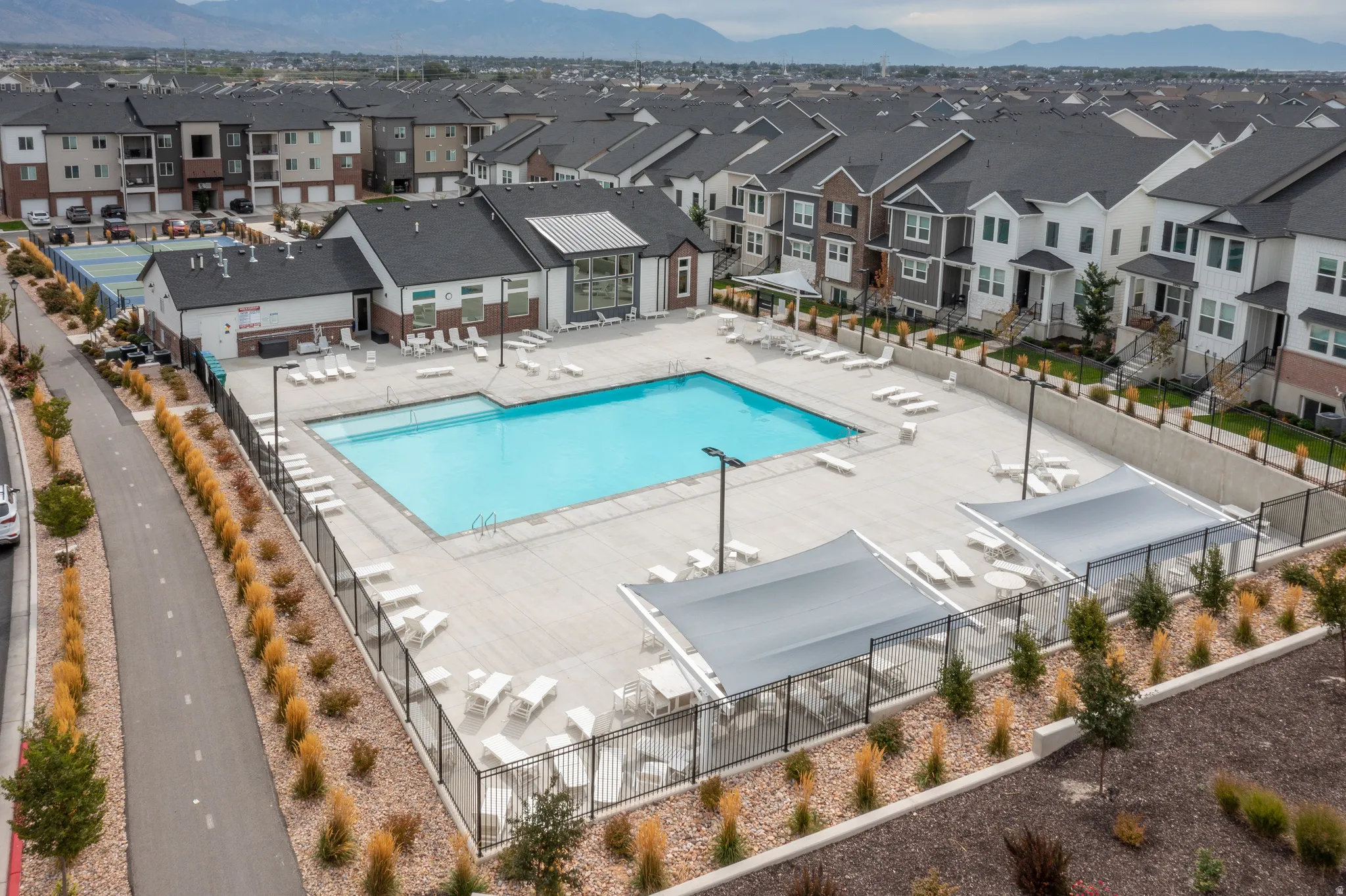 Expansive outdoor swimming pool with surrounding lounge areas, shade structures, and adjacent clubhouse