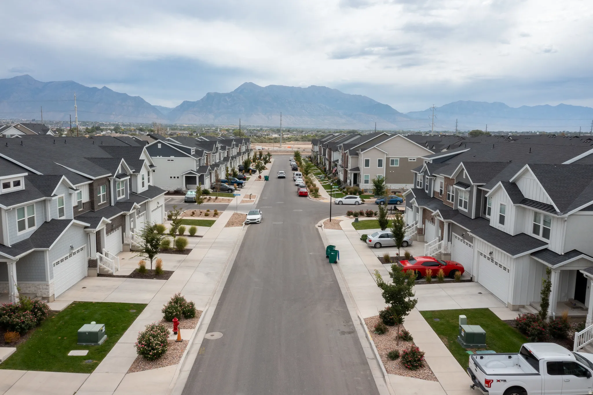 Community setting with mountain backdrop featuring a tree-lined street, uniform sidewalks, and well-maintained streetlights