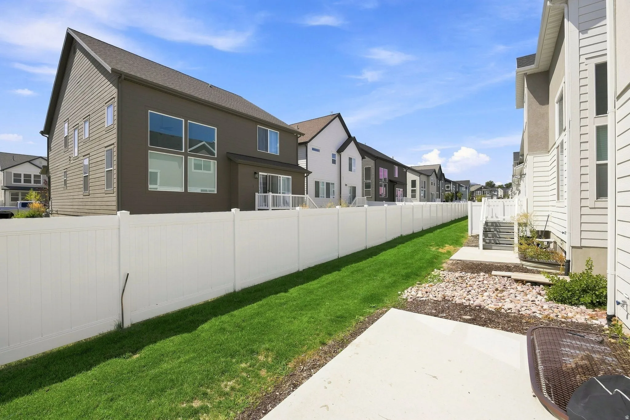 Concrete patio with rock landscaping, white vinyl fencing, and a manicured lawn