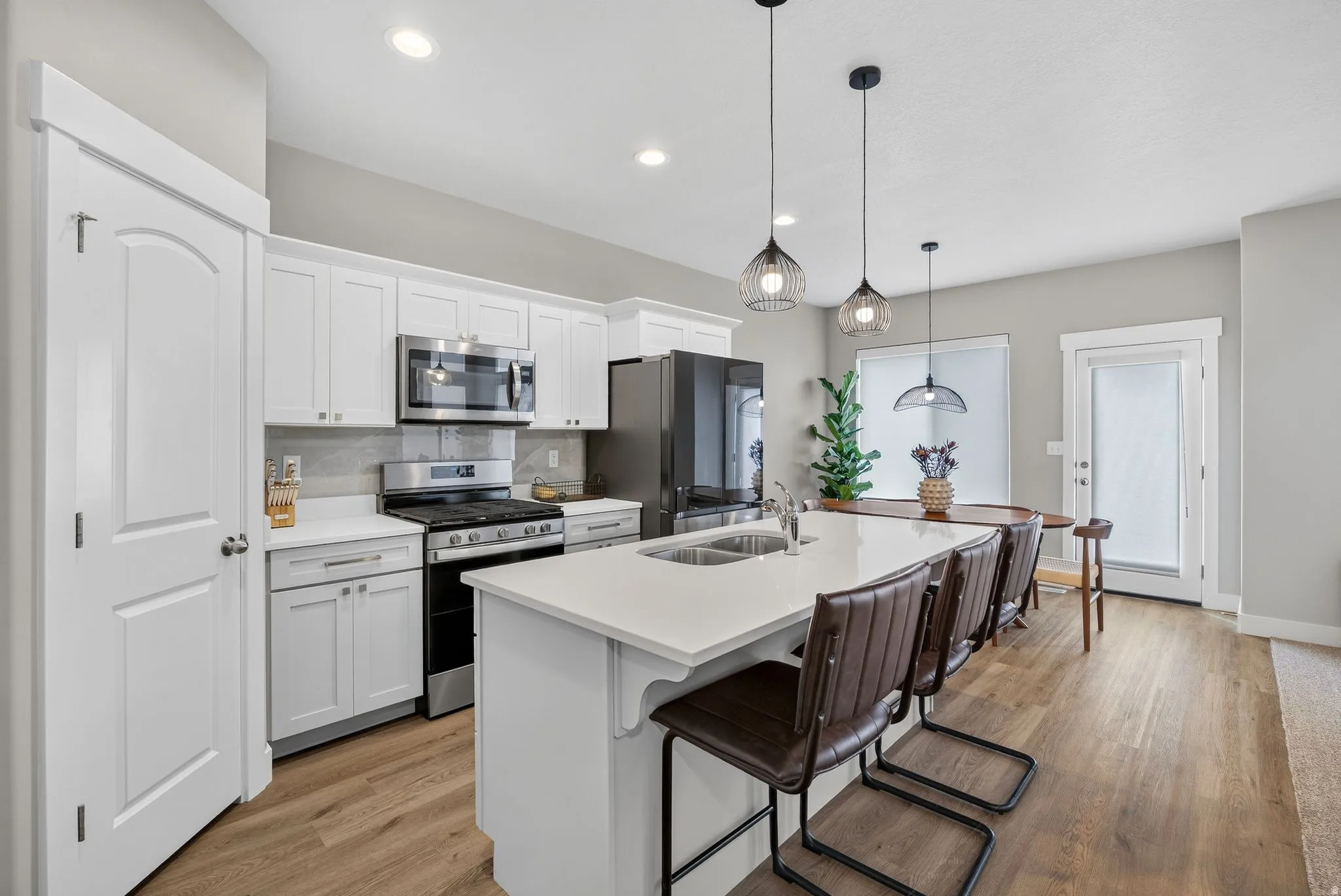 Kitchen featuring white cabinetry, stainless steel appliances, a center island with sink, and wood-finish flooring