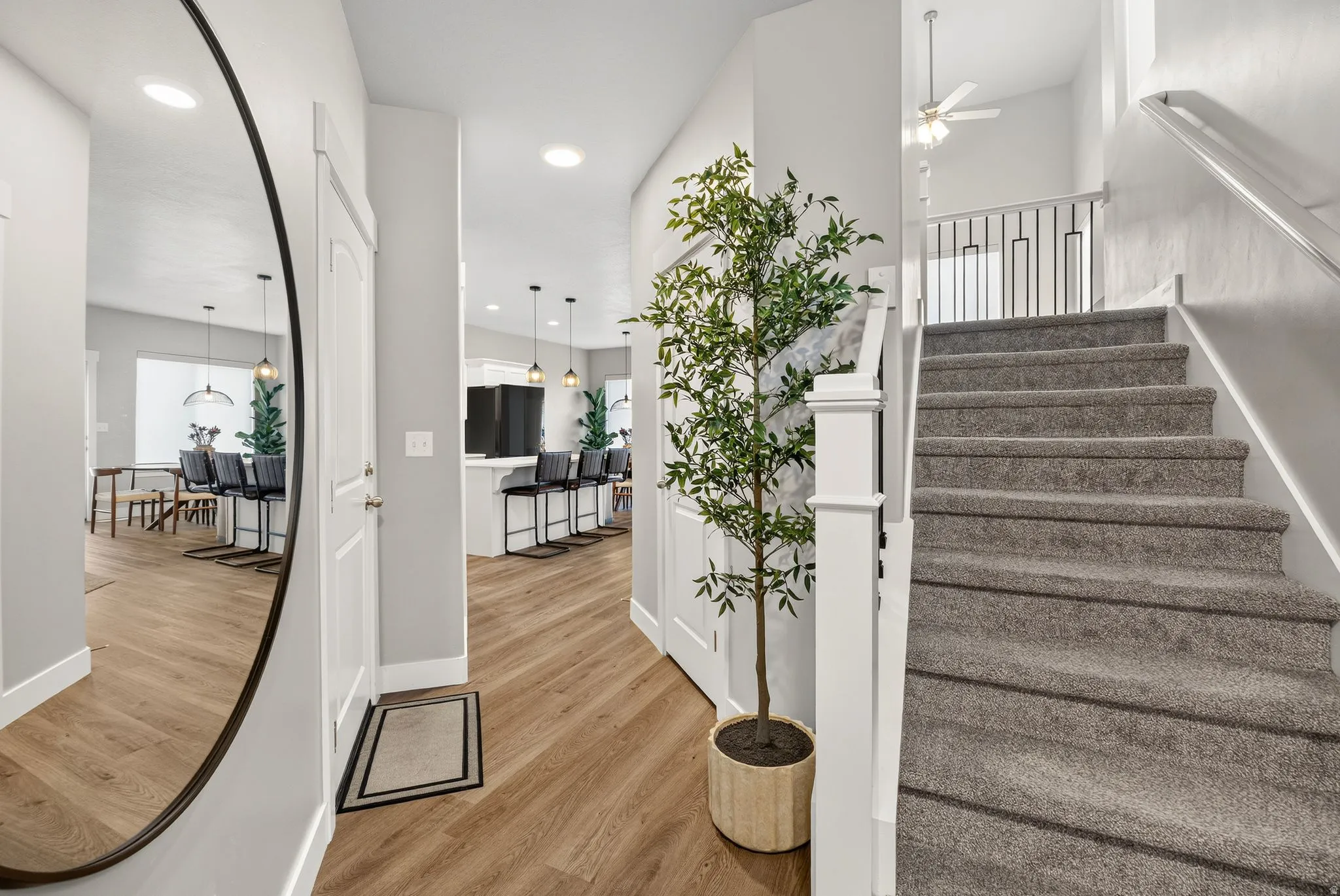 Wood-finish flooring, recessed lighting, white interior doors, staircase with gray carpet and white railing, black metal balusters