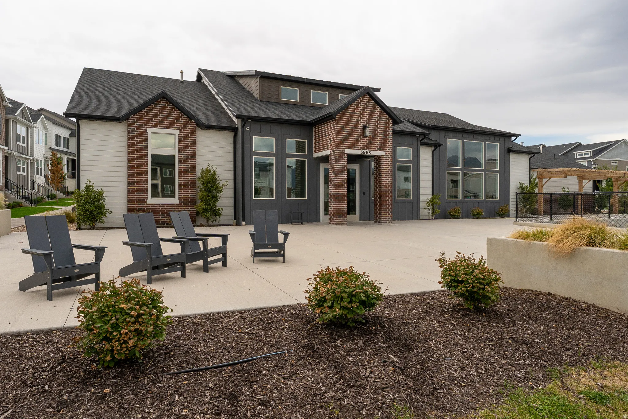 Contemporary architectural style with brick and siding facade, large window arrays, dark shingled roof, and an expansive concrete patio