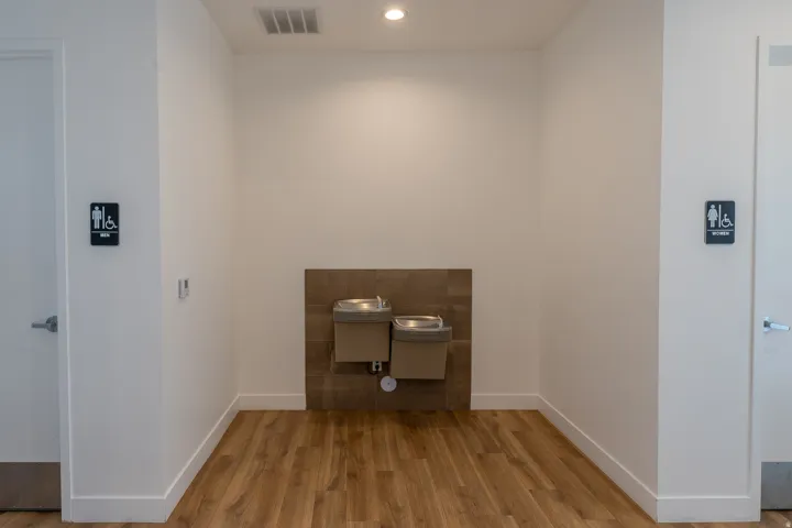 Wood-finish flooring, two stainless steel water fountains, recessed ceiling lighting, and white baseboards
