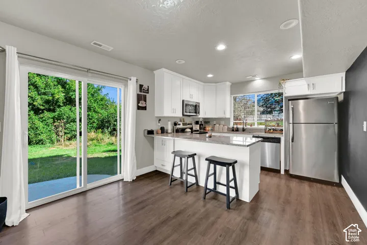 Kitchen featuring stainless steel appliances, white cabinetry, a center island with seating, and wood-finish flooring