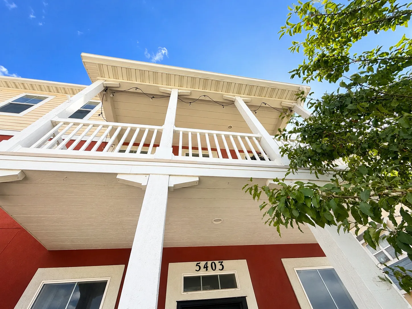 Two-story exterior with a red and beige facade, featuring a prominent balcony with white railings and columns, and multiple windows