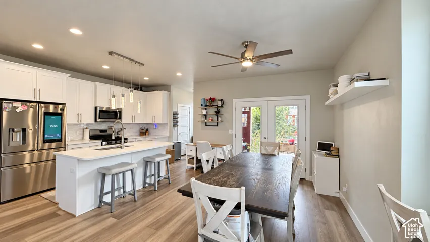 Kitchen and dining area featuring wood-finish flooring, white cabinetry, stainless steel appliances, and a kitchen island with seating