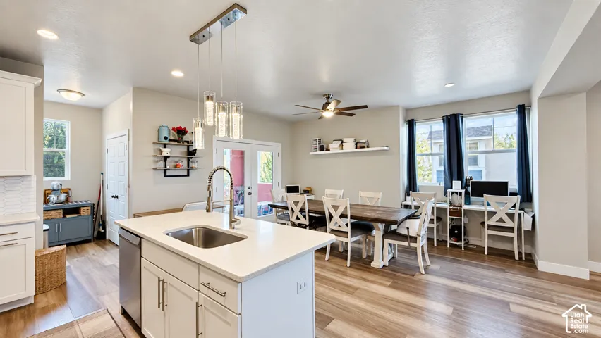 Open-concept living area featuring a kitchen island with sink, pendant lighting, wood-finish flooring, and a ceiling fan