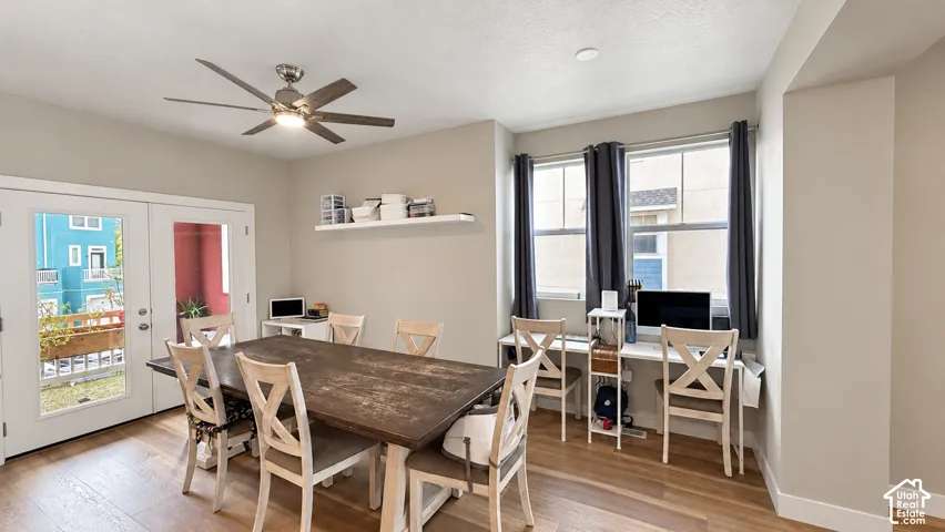 Wood-finish flooring, ceiling fan, white floating shelves, dual windows, and exterior French doors