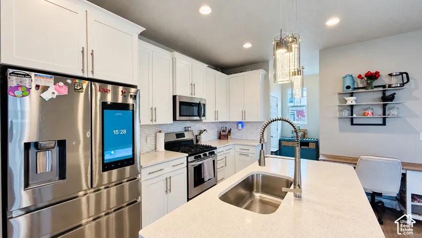 White shaker cabinetry, stainless steel appliances, mosaic tile backsplash, built-in task lighting, and a kitchen island with an integrated sink